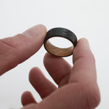 man holding a close up of a tungsten and wood wedding ring for men